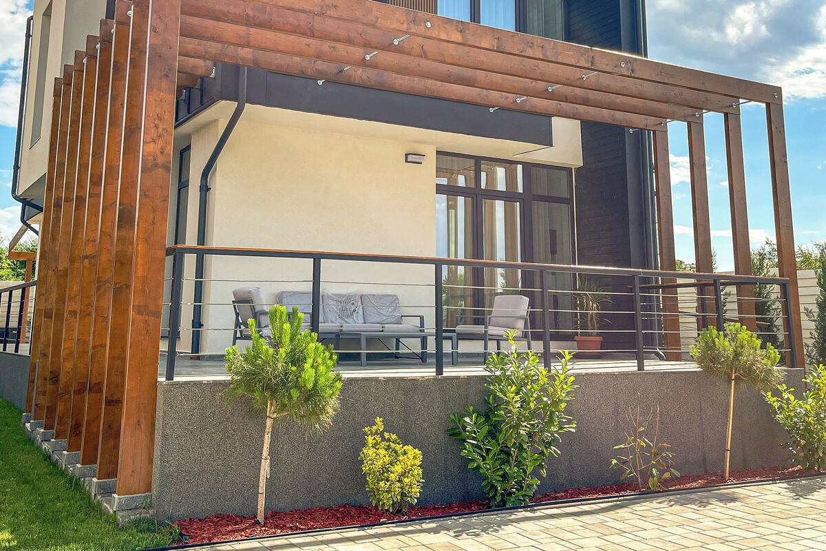A modern two-story house with a wooden pergola, a balcony, and a small garden area.