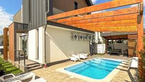 Une maison moderne dotée d’une piscine, d’un espace salon extérieur et d’une pergola.