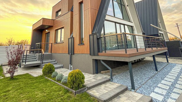 Une maison moderne à deux étages, dotée d’un toit en pente, de grandes fenêtres et d’une façade en bois.
