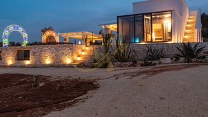 A modern house with a stone facade, a glass entrance, and a circular light arch. - TD ApulianRetreat Scenic Villa with hammam & pool (Costa Merlata)