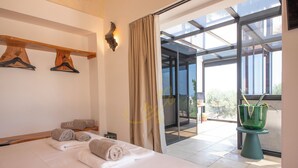 A hotel room with a bed, towels, a wooden shelf with hangers, a wall-mounted light, and a view of the outdoors through a glass door. - TD ApulianRetreat Scenic Villa with hammam & pool (Costa Merlata)