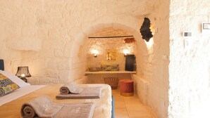 A cozy room with a stone wall, a bed with towels, a lamp, and a small shelf with decorative items. - TD ApulianRetreat Sea view trullo w/heated pool (Costa Merlata)