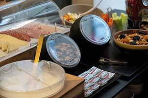 Buffet variado com diversos alimentos, incluindo um espaço com carnes, um recipiente com frutos secos e uma saladeira.