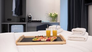 A hotel room with a neatly made bed, a tray with fruit and juice, and a stack of towels. - ATHENS RETRO (Athens)