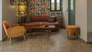 A modern living room with a patterned wallpaper, a sofa, a coffee table, and a rattan chair. - ATHENS RETRO (Athens)