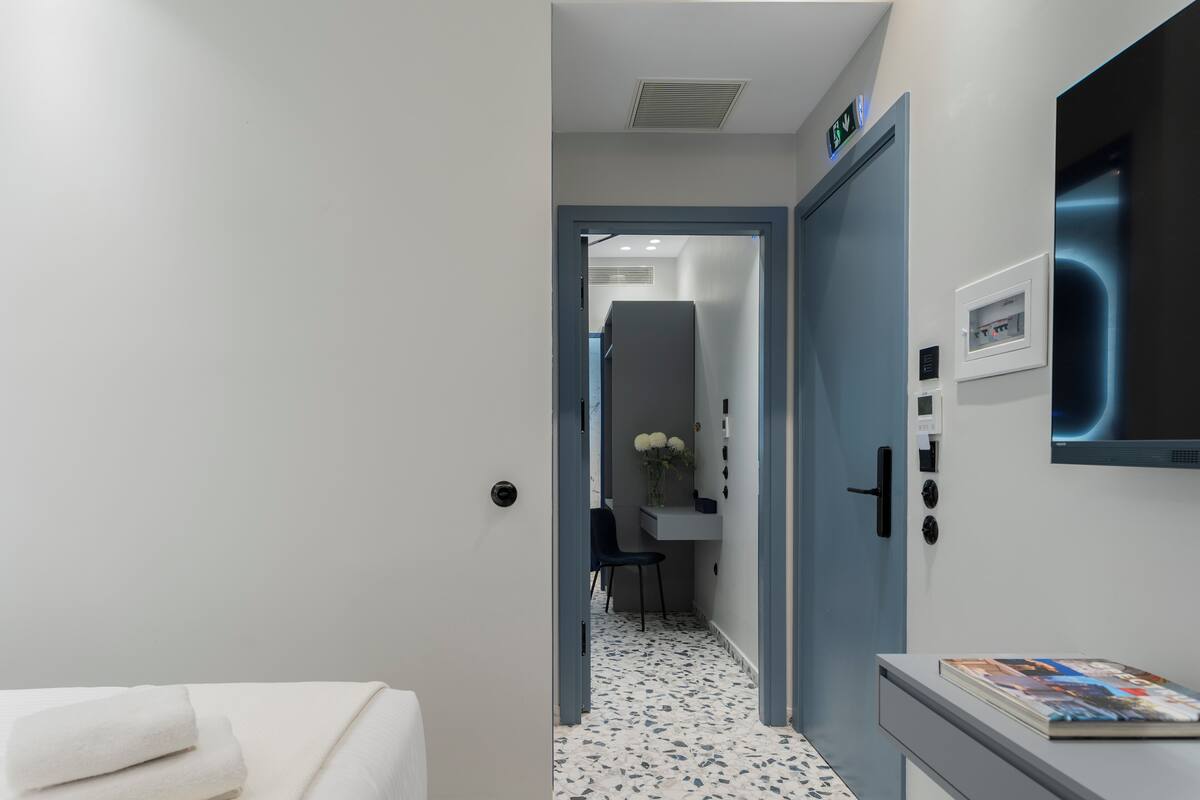 A modern hotel corridor with a white door, a reception desk, and a chair.
