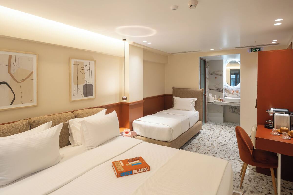A hotel room with two beds, a desk, and a chair. There is a book on the bed and a bathroom visible through an open door.