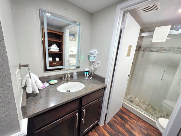 Une salle de bain moderne dotée d’un grand miroir, d’un lavabo, d’un sèche-cheveux et d’une douche à parois de verre.