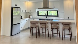 A modern kitchen with white cabinets, a built-in island with bar stools, and a large window. - 3-br Villa With Private Pool in Punta Cana Village (Punta Cana)