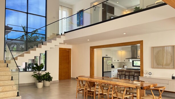A spacious kitchen with white cabinets, a wooden dining table, and a glass staircase leading to an upper level. - 3-br Villa With Private Pool in Punta Cana Village (Punta Cana)