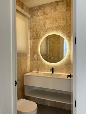 A bathroom with a marble wall, a round mirror, a white sink, and a toilet.
