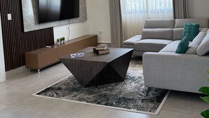 A modern living room with a flat-screen TV mounted on the wall, a grey sofa, a coffee table, and a patterned rug. - 3-br Villa With Private Pool in Punta Cana Village (Punta Cana)