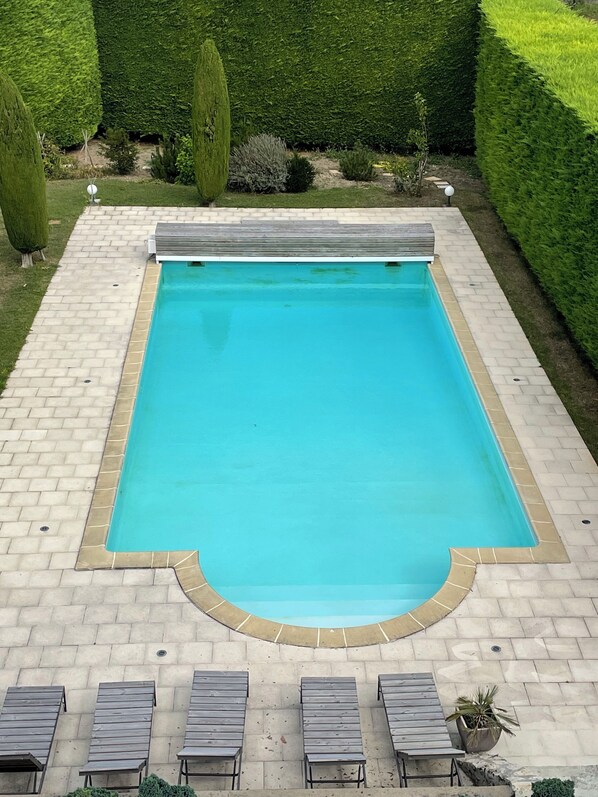 Une piscine rectangulaire bordée de carreaux, entourée d’une terrasse en briques. Des chaises longues sont alignées le long du bord de la piscine.