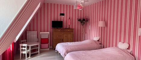 A bedroom with two beds, a desk, a chair, a TV, and a wardrobe.