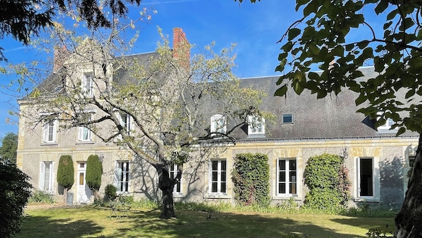 A large stone building with a symmetrical facade, multiple windows, and a central tree.