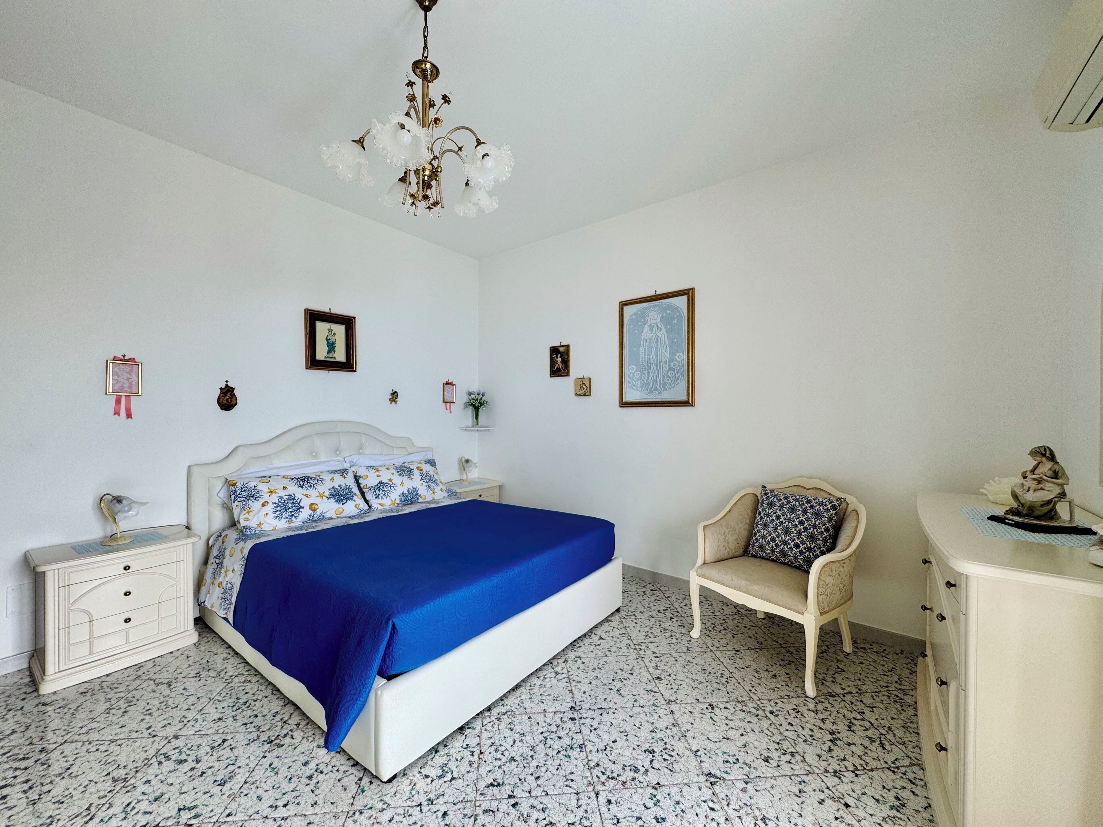 A bedroom with a bed, nightstands, a chair, a dresser, and a chandelier.