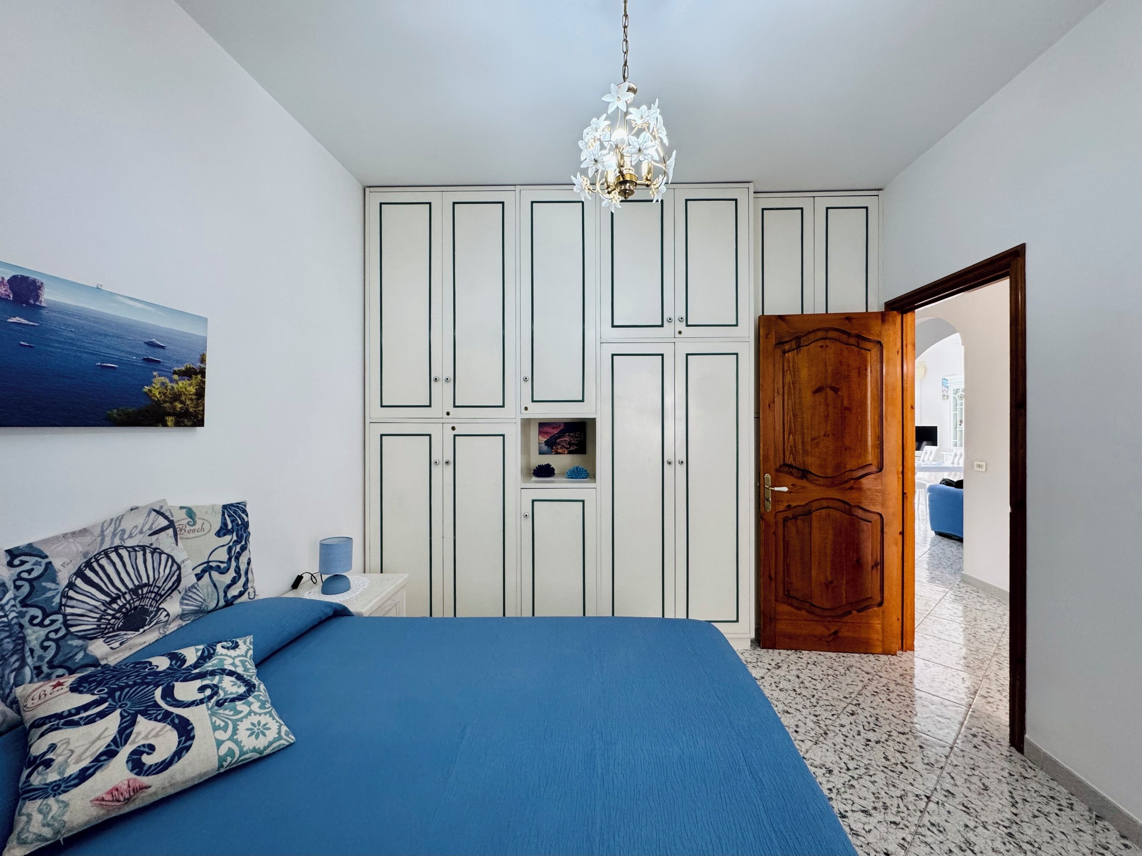 A bedroom with a bed, a wardrobe, a chandelier, and a door leading to another room.