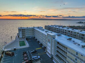 Ein Hotel mit mehreren Etagen, einem Parkplatz und Blick auf das Meer bei Sonnenuntergang.