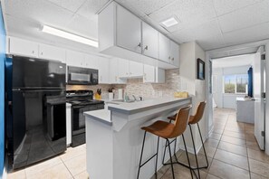 Une cuisine moderne avec des meubles blancs, un îlot central doté de tabourets de bar et une vue sur l’extérieur.