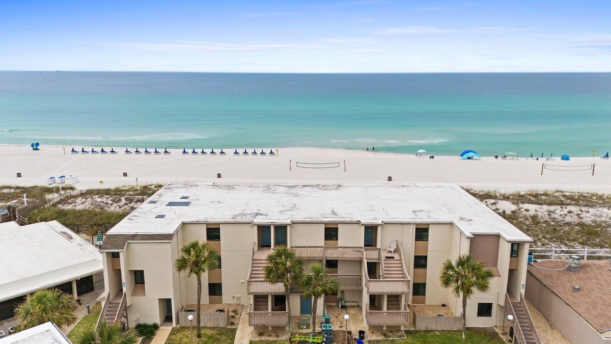 A beachfront hotel with a view of the ocean, a sandy beach, and a pool area.