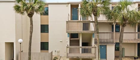 A multi-story residential building with balconies, a clear sky, and palm trees.