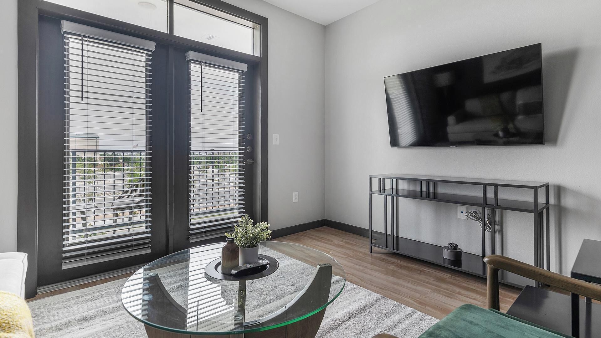 Een moderne woonkamer met een glazen tafel, een open haard en een aan de muur bevestigde televisie.