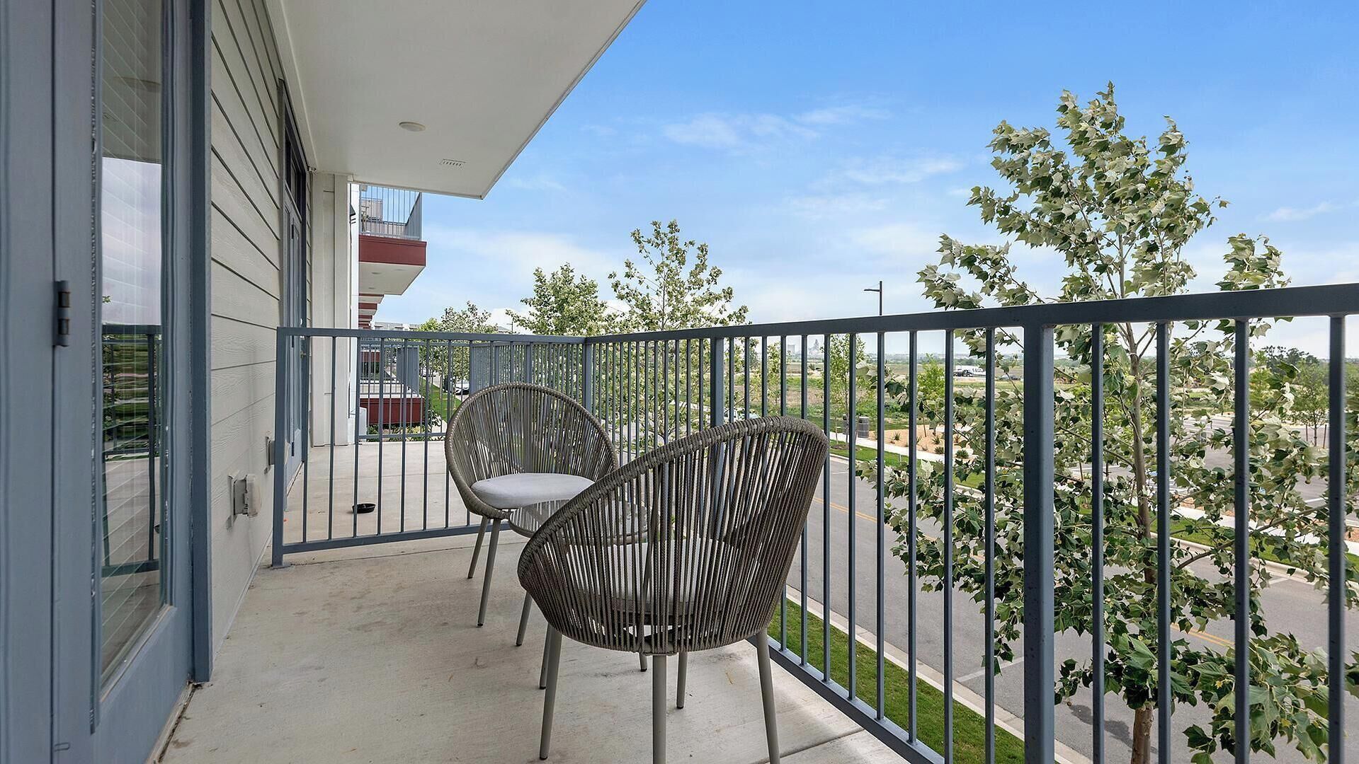 Een balkon met twee rieten stoelen en uitzicht op een woonwijk.