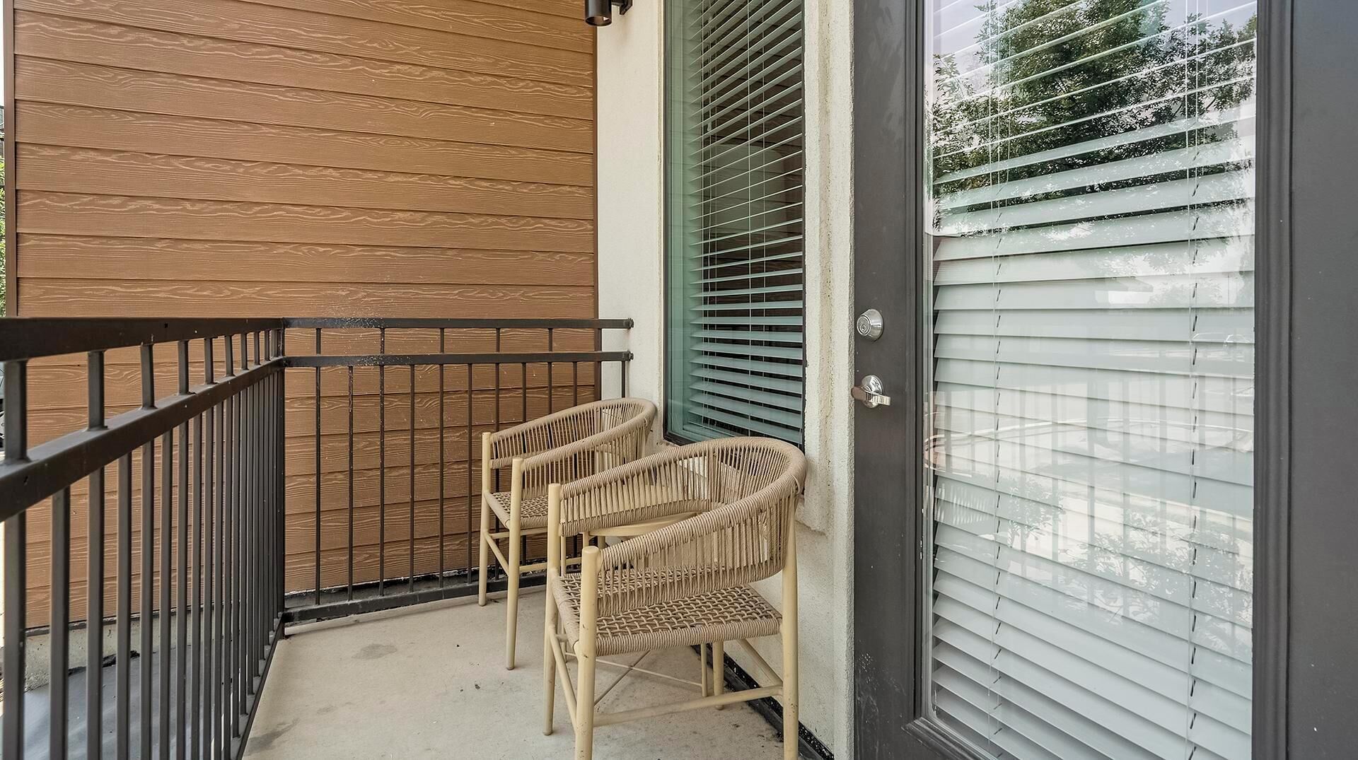 A balcony with two wicker chairs and a metal railing.