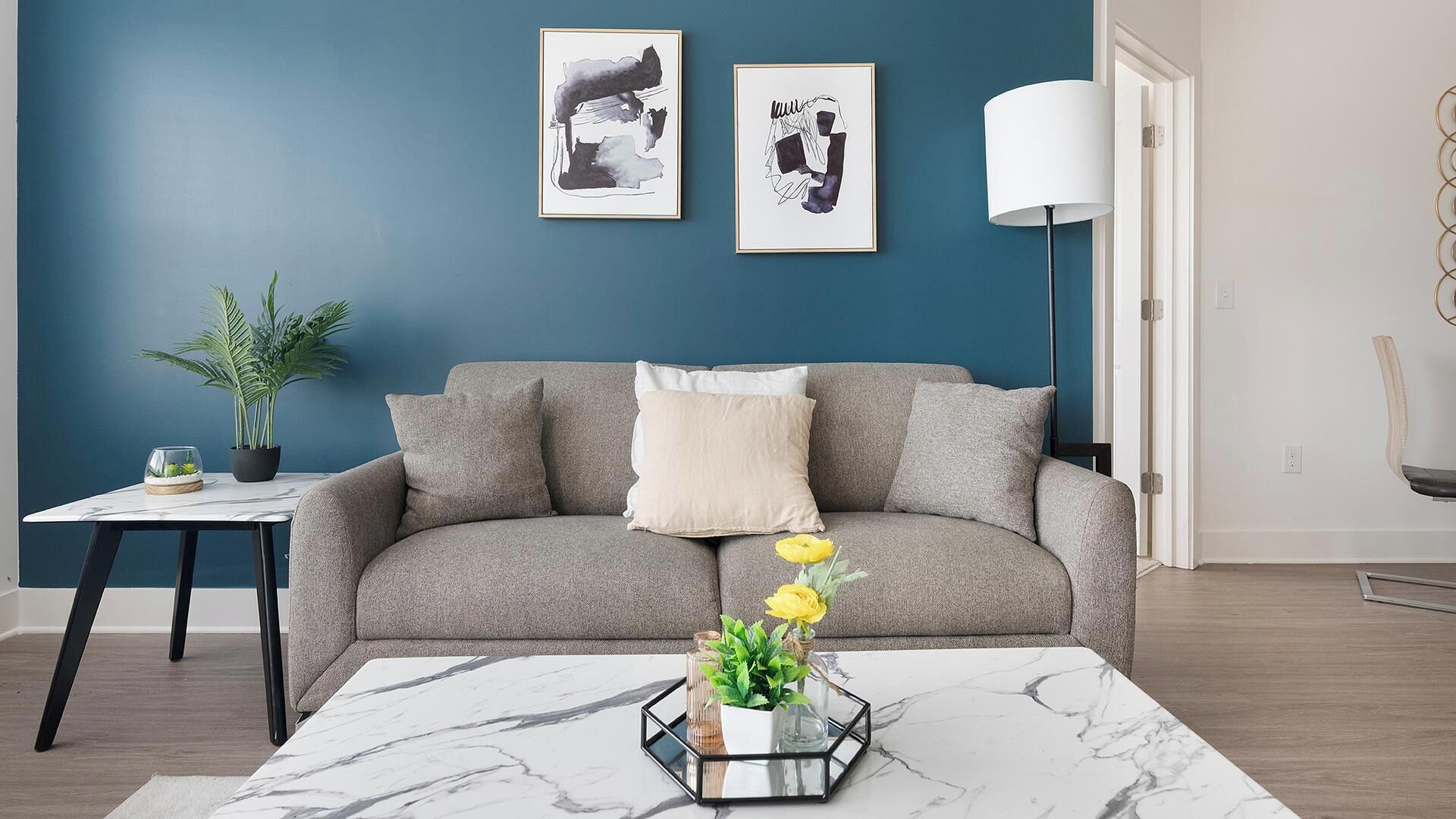 A living room with a grey sofa, a small side table with a plant, and a coffee table with a vase of flowers.