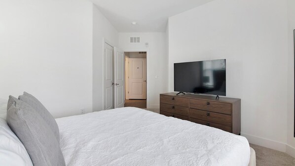 A bedroom with a bed, a TV on a dresser, and a door leading to another room. - Landing | Beautiful 1BD, Yoga Studio, Pool (Athens)