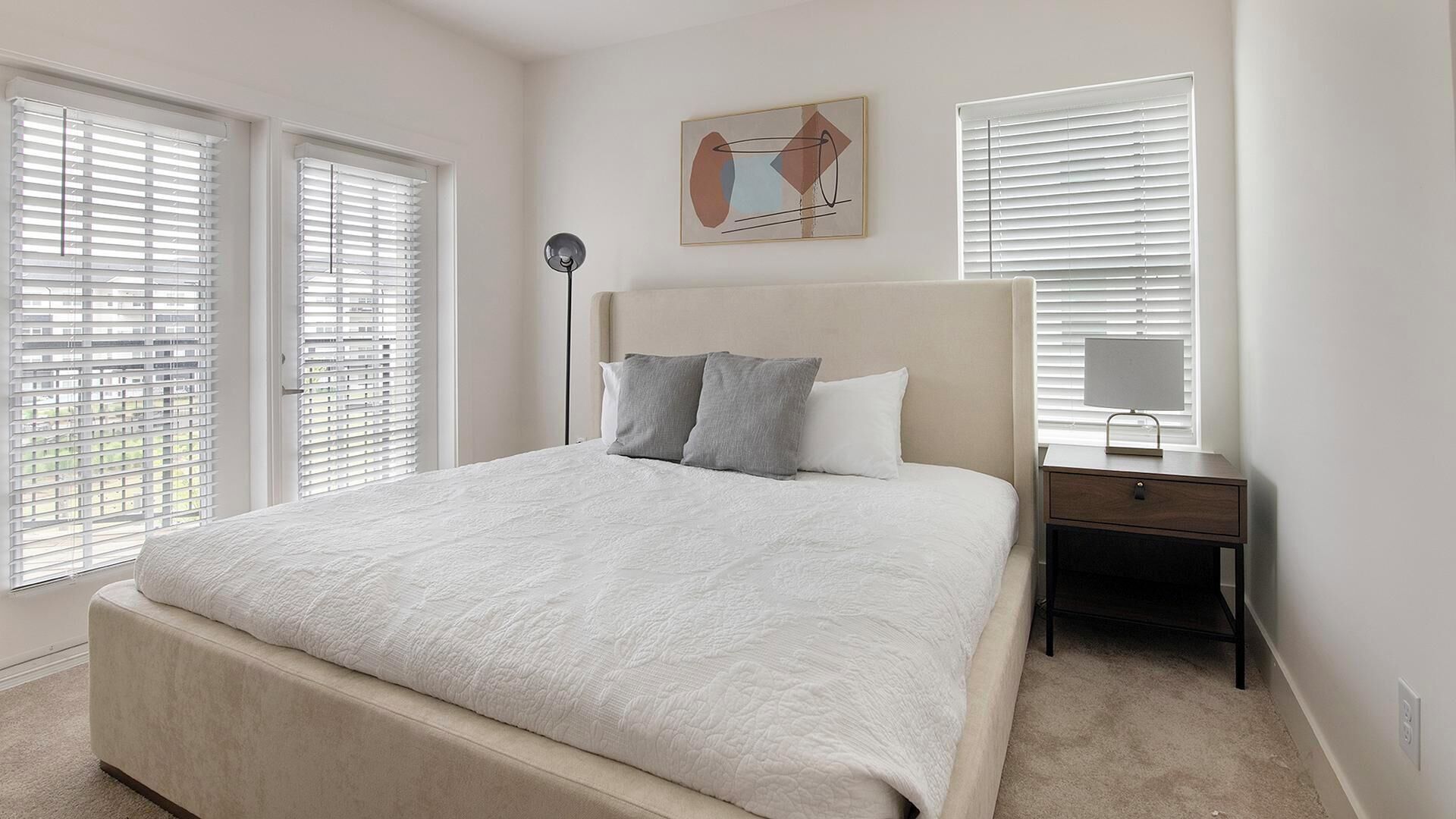A bedroom with a large bed, two bedside tables, and a floor lamp.