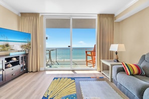 Ein Hotelzimmer mit Balkon, Fernseher, einer Couch, einer Lampe und einem Teppich.