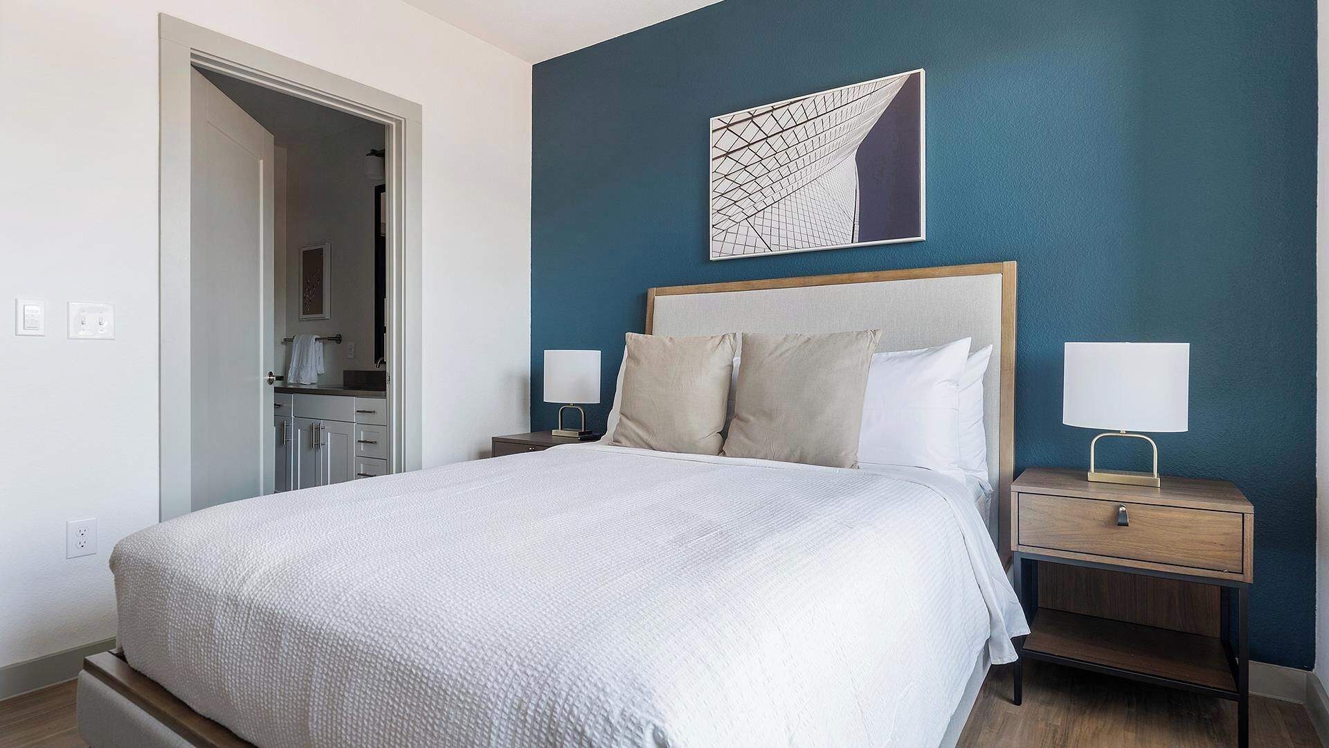 A neatly made bed with a headboard, two bedside tables with lamps, and a wall art piece above the bed.