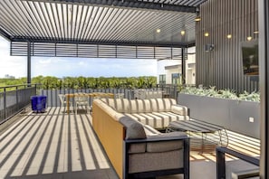 A rooftop terrace with a modern design, featuring a seating area with a sofa and chairs, a small table, and a blue pot.