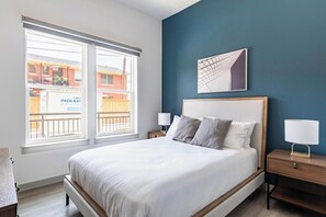 Ein Schlafzimmer mit einem Bett, zwei Nachttischen, einem Fenster mit Blick auf ein Gebäude und einem Wandbild.