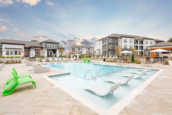 A modern hotel with a large outdoor swimming pool, lounge chairs, and a well-maintained garden area.
