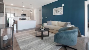 Una sala de estar moderna con una pared azul de acento, un sofá, una mesa de centro y una cocina al fondo.