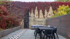 Une terrasse extérieure avec un sol à carreaux, un mur de briques et une rangée de chaises noires et une table.