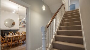 Un escalier recouvert d’une moquette beige et doté de balustrades blanches, menant à une pièce comprenant un coin repas et une bibliothèque.