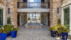 A courtyard with a central fire pit, stone walls, and potted plants. - Landing | Modern 1BD, Game Room, Gym (Allen)