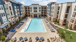 A multi-story hotel with a central swimming pool surrounded by lounge chairs and sunbeds.