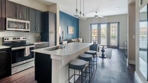Uma cozinha moderna com armários escuros, eletrodomésticos de aço inoxidável, uma ilha central com banquetas e uma janela grande que oferece iluminação natural.