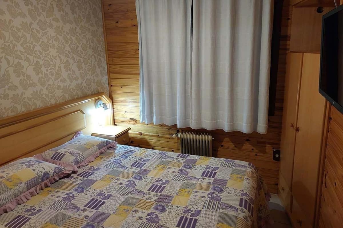 A wooden cabin room with a bed, a nightstand, a radiator, and a wooden wardrobe.