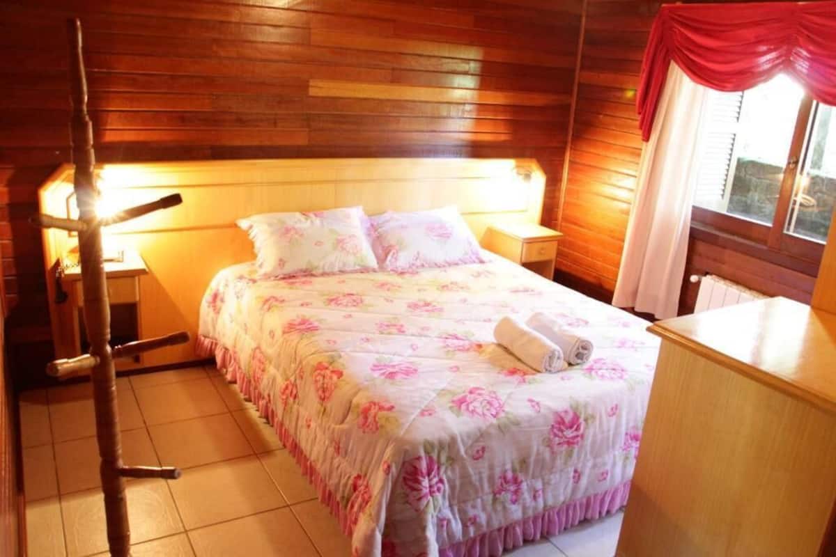 A wooden-paneled bedroom with a bed, nightstands, and a window with curtains.