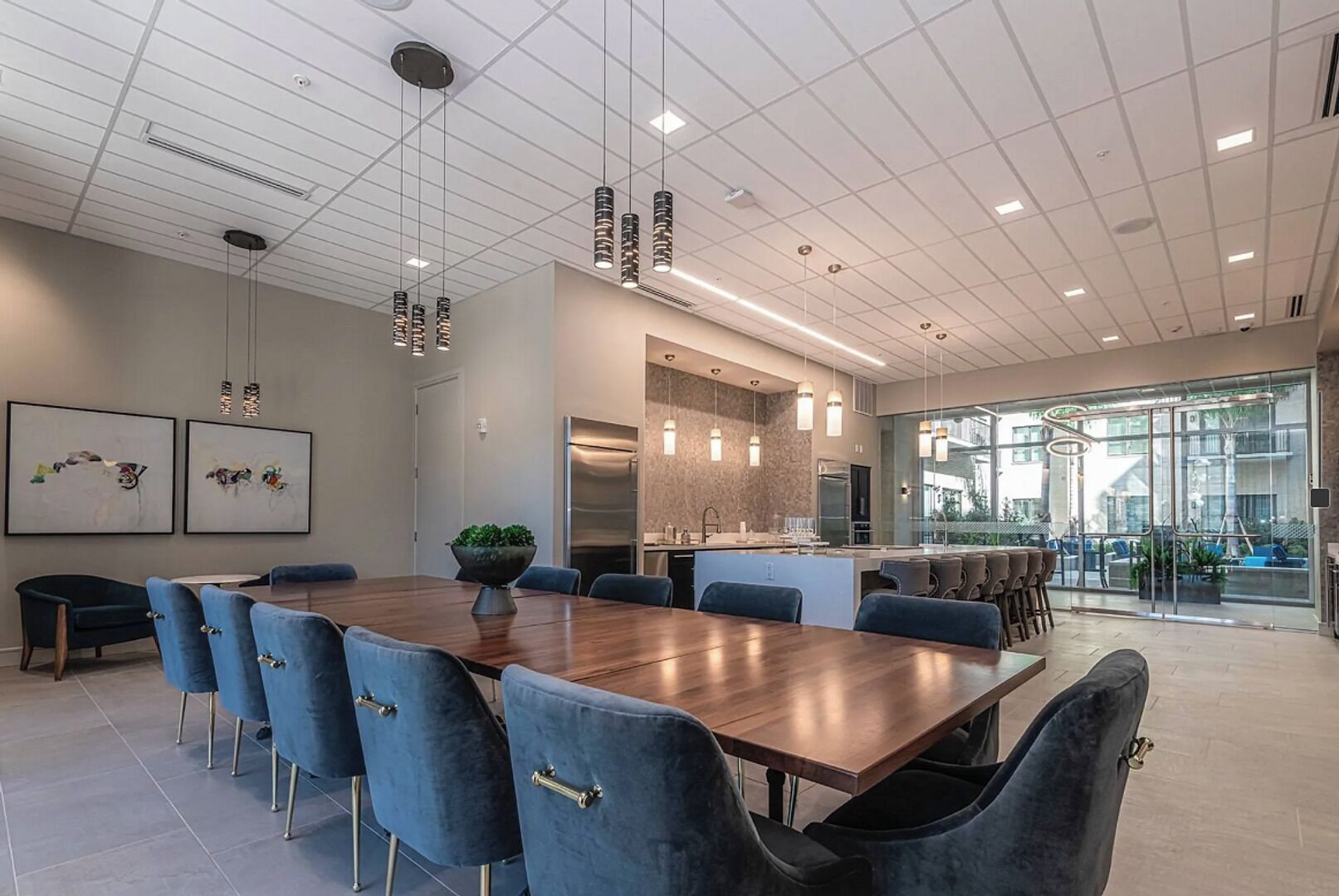 A modern meeting room with a long wooden table, blue upholstered chairs, and pendant lighting.