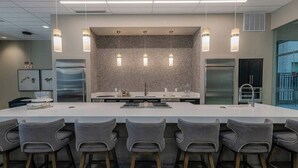 Une cuisine moderne dotée d’un îlot central, de tabourets de bar, de luminaires suspendus et d’appareils électroménagers en acier inoxydable.