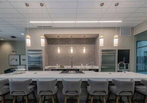 Una cucina moderna con isola centrale, sgabelli da bar, illuminazione a sospensione ed elettrodomestici in acciaio inossidabile.