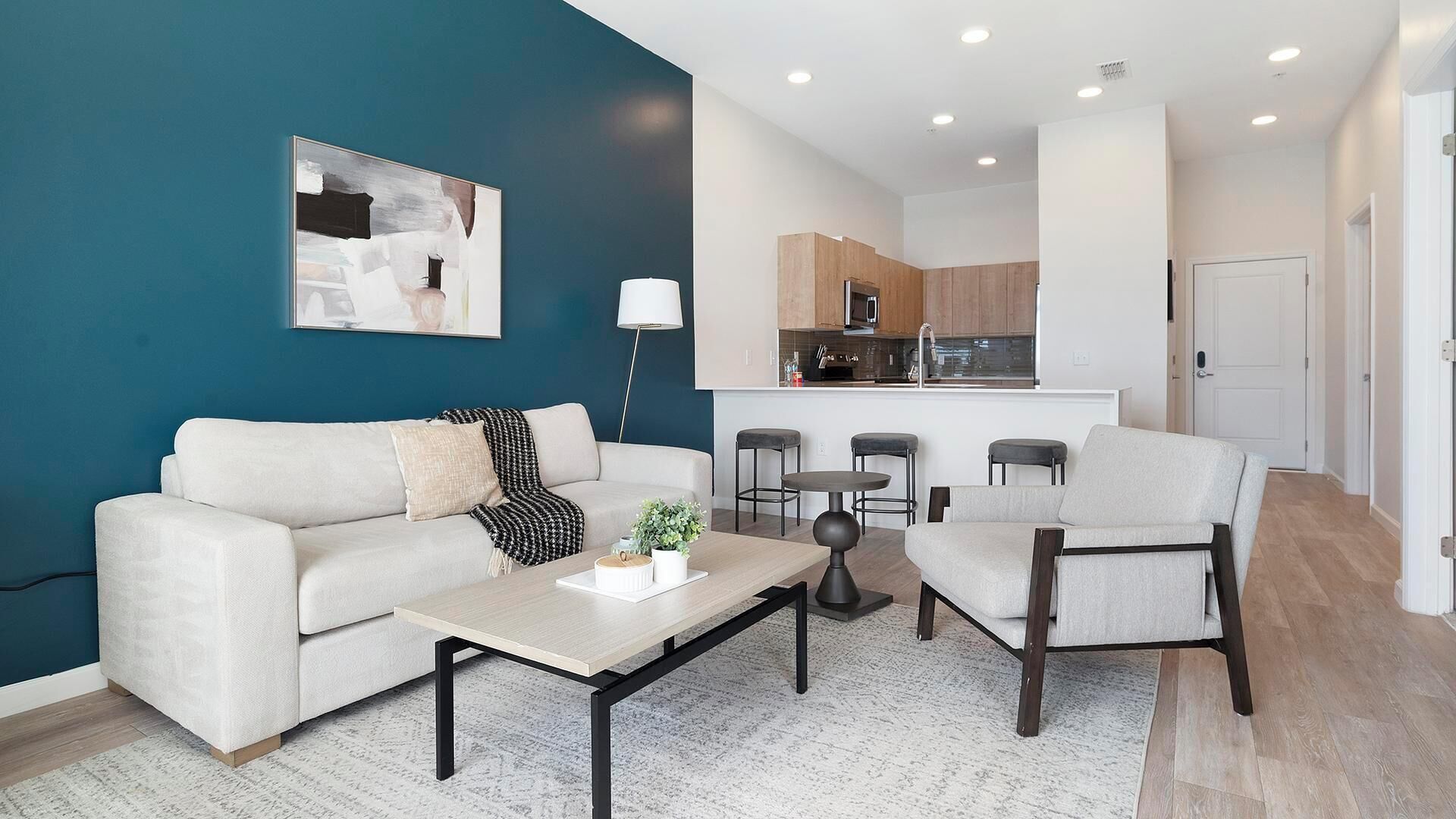 A modern living room with a sofa, armchair, coffee table, and a painting on the wall.