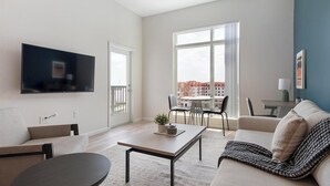 Uma sala de estar moderna com televisão de tela plana, um sofá, uma mesa de centro e uma área de jantar com cadeiras e uma mesa.