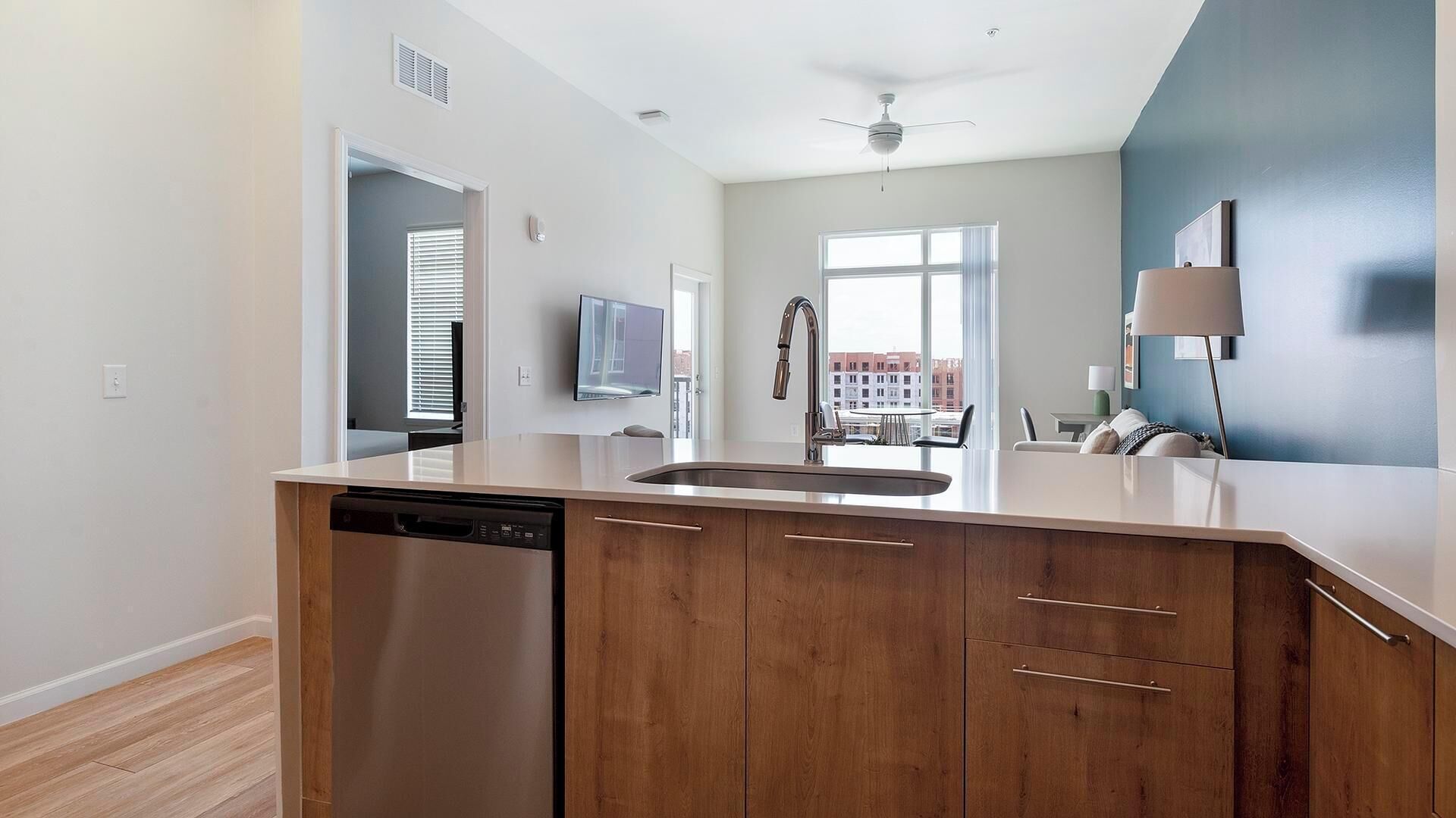 A modern kitchen with a dishwasher, wooden cabinets, a stainless steel sink, and a ceiling fan.
